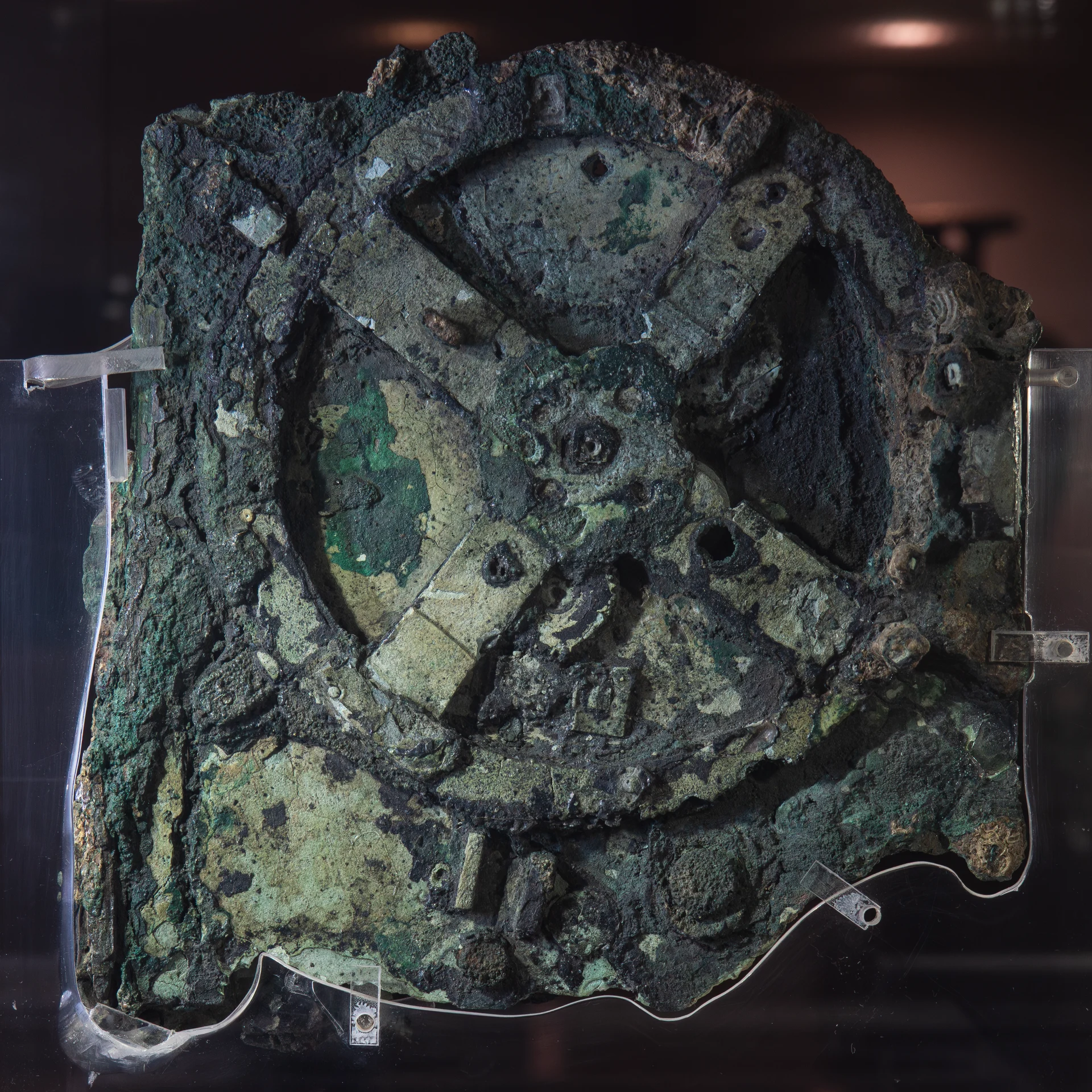 Fragmento de bronce corroído de color verde en el que se ve una gran rueda dentada